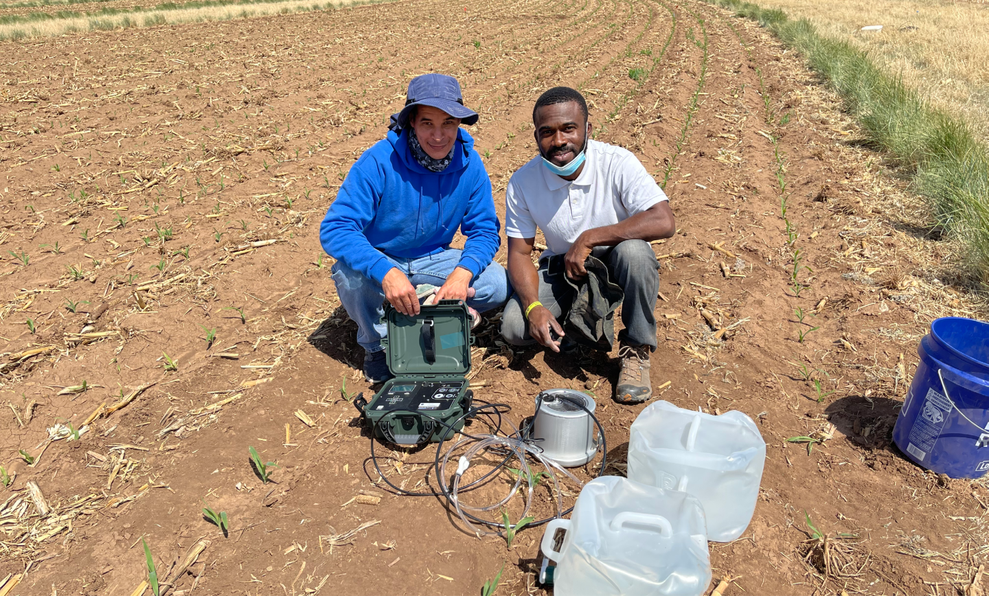 Two scientists kneel in a field with equipment.