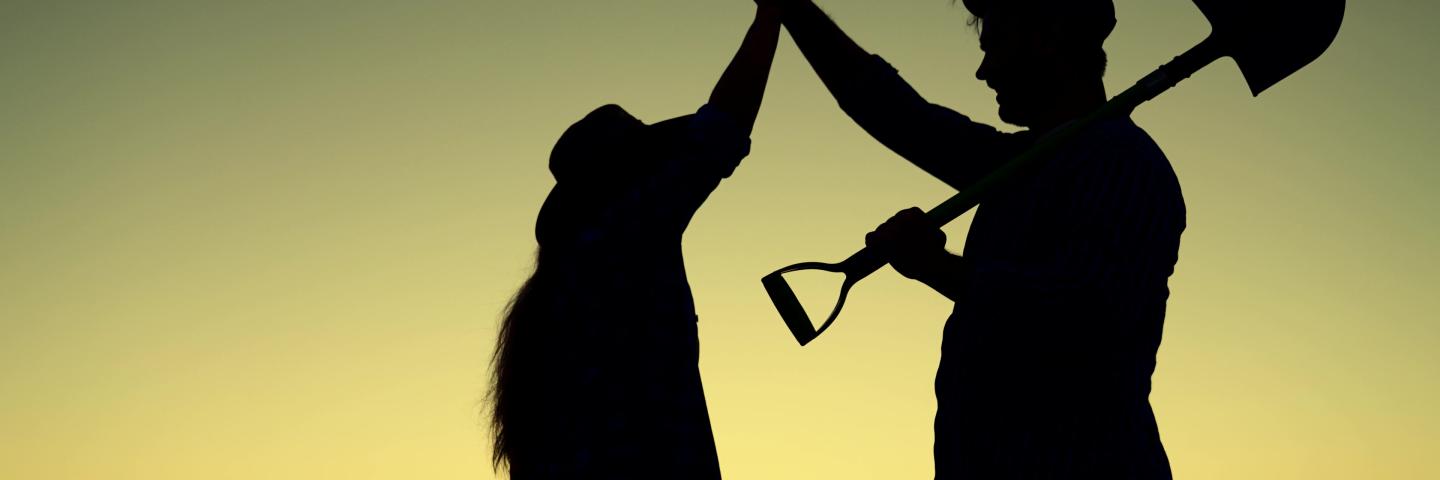 Silhouette farmers woman and man with shovel, meet in field at sunrise and shake hands.