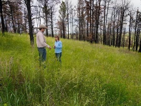 NRCS employee and landowner walk an area with burned trees.
